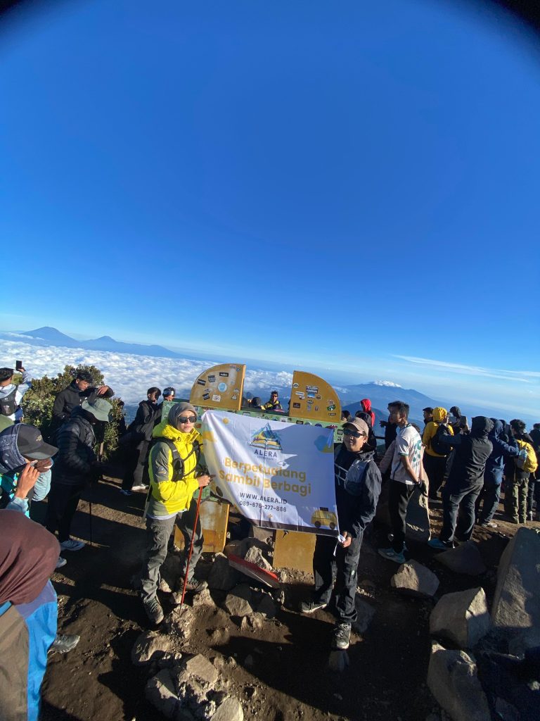Pendaki ceria menikmati pemandangan dengan Paket Porter Wekas Alera Adventure. Judul: Paket Porter Wekas Ceria Alera Adventure Keterangan: Senyum merekah di puncak berkat kehadiran porter kesayangan! Dijamin bikin pendakian makin syahdu dan bebas drama ransel berat. Deskripsi: Sebuah gambar yang menangkap kegembiraan pendaki di ketinggian, menikmati momen tanpa beban berkat layanan Paket Porter Wekas dari Alera Adventure, menggambarkan kemudahan dan kesenangan dalam mendaki gunung.